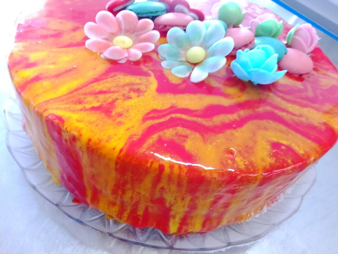 Torta gelato con glassa marmorizzata rosa e arancio, fiori e macaron