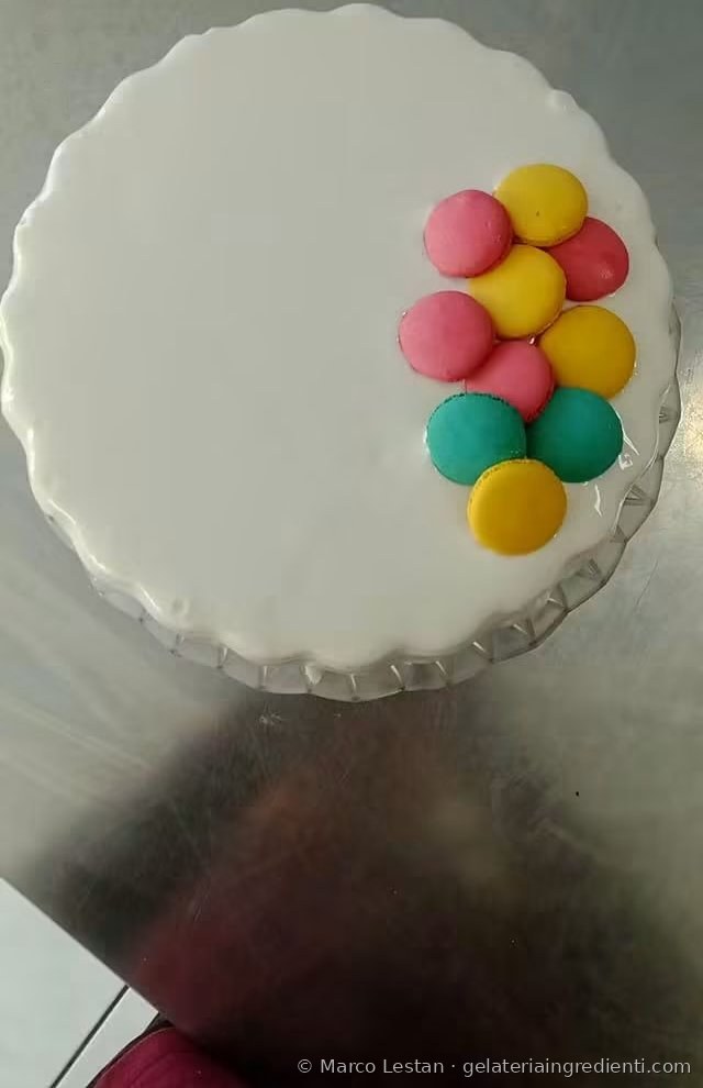 Torta gelato con glassa bianca e macaron colorati rosa, gialli e turchesi