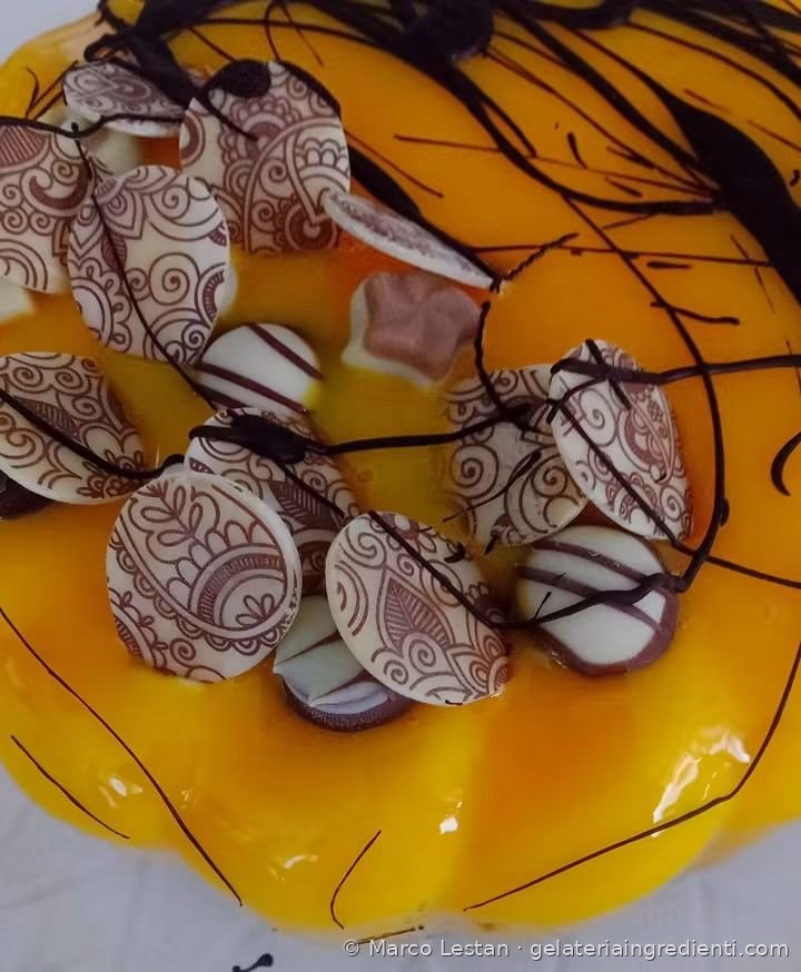 Dettaglio di torta gelato con glassa arancione, dischi di cioccolato decorato a motivi paisley e fili di cioccolato