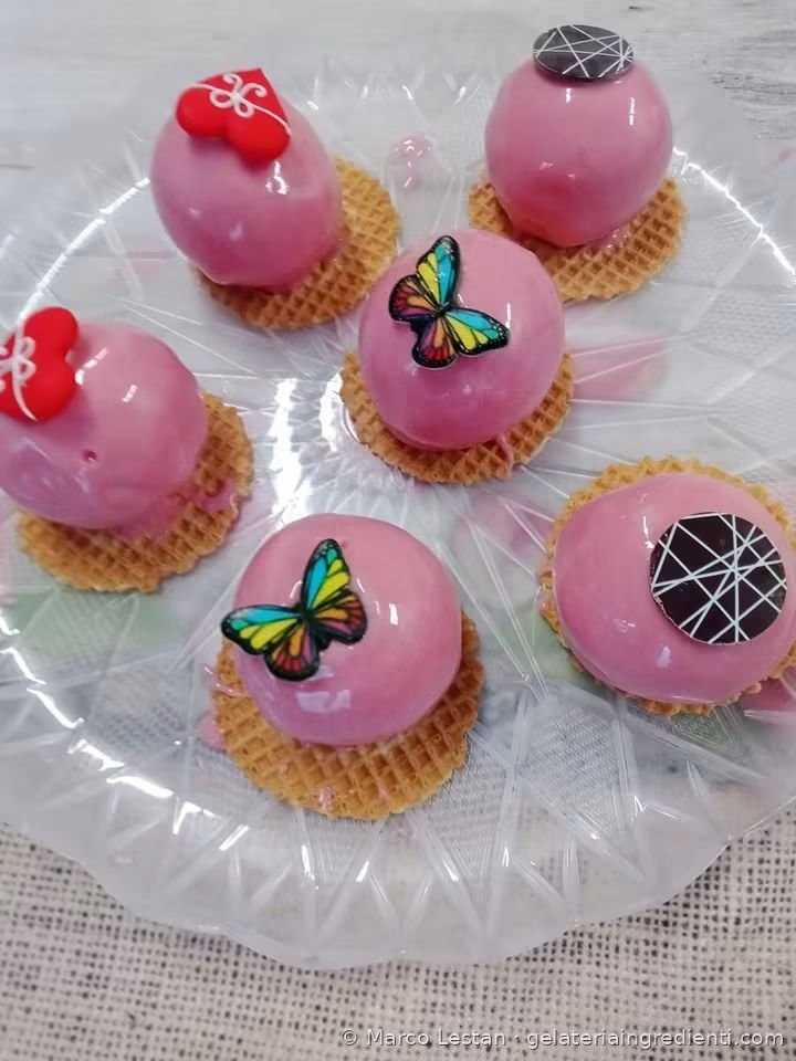 Monoporzioni di gelato glassate rosa su cialda, con cuori rossi, farfalle e dischi di cioccolato