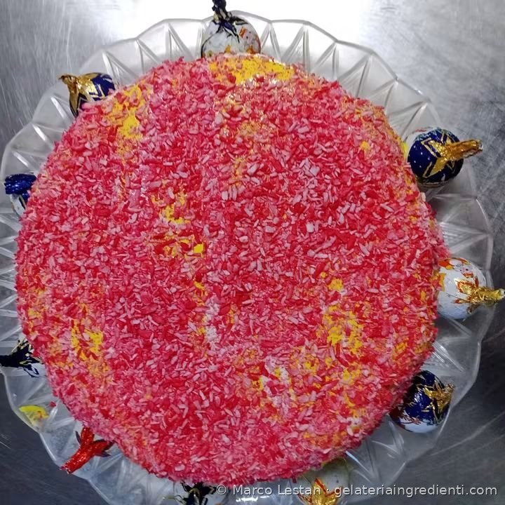Torta gelato ricoperta di granella rosa e rossa, circondata da cioccolatini incartati