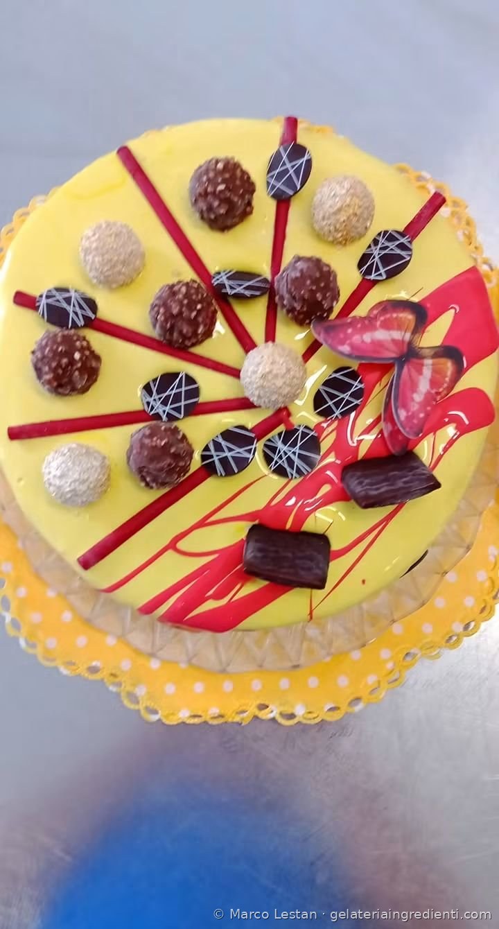 Torta gelato con glassa gialla, praline, bastoncini rossi, dischi di cioccolato e farfalla