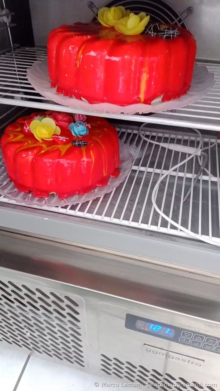 Due torte gelato con glassa a specchio rossa appena glassate, sui ripiani di un frigorifero