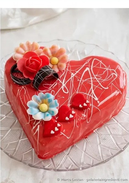 Torta gelato finita a forma di cuore con glassa a specchio rossa, fiori di zucchero e decorazioni