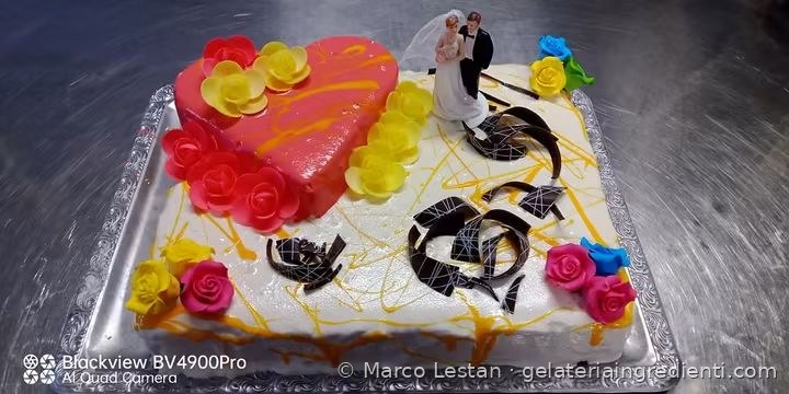Torta rettangolare con cuore rosa, rose colorate e scaglie di cioccolato vista da un'altra angolazione